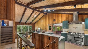 A spacious kitchen with wooden beams, a large island, and a stainless steel stove.