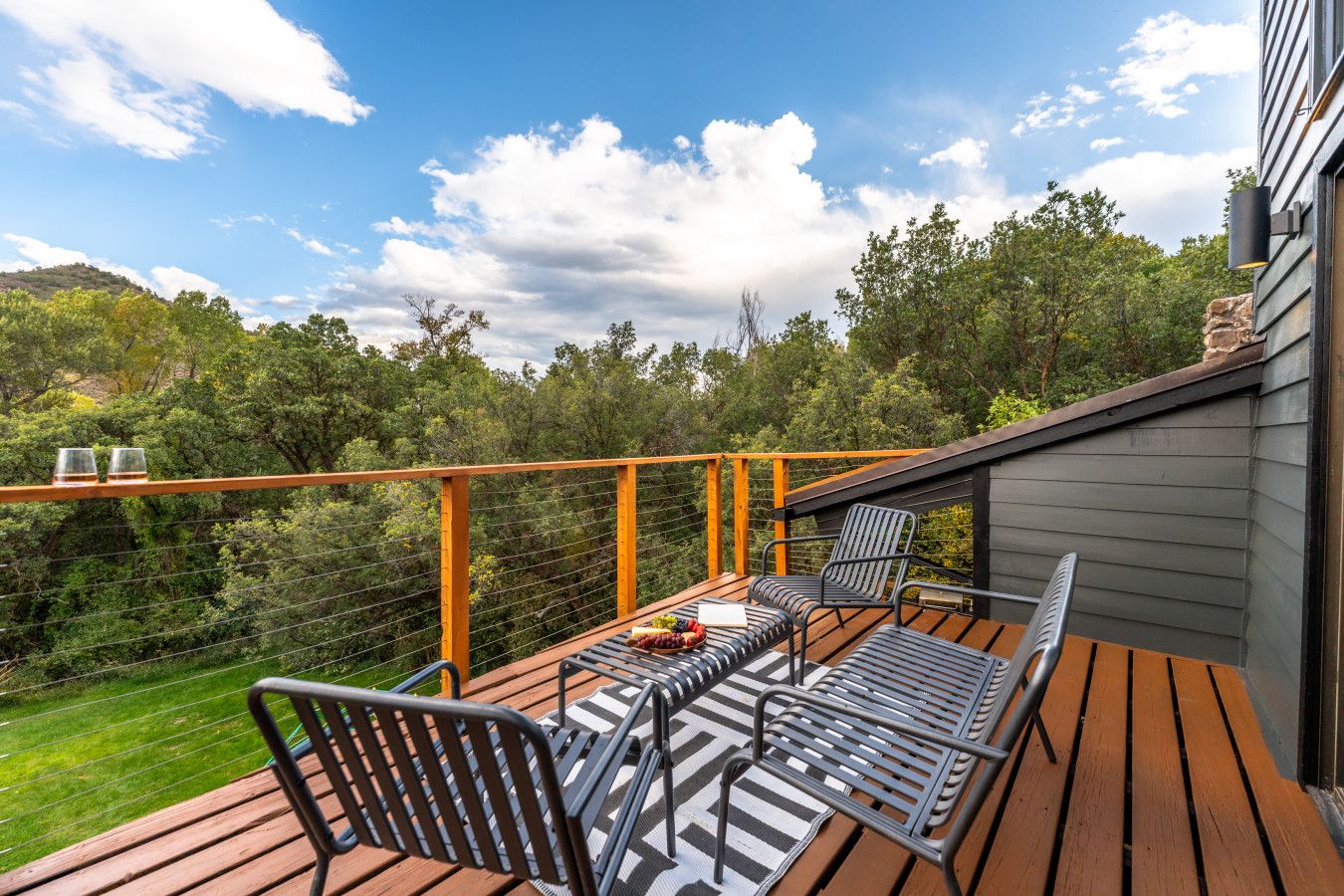 Una terraza de madera con mobiliario exterior, barandilla y vistas a un área boscosa.