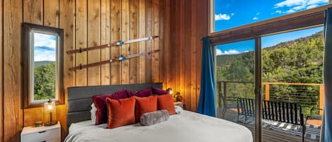 A bedroom with a large bed, wooden walls, a window, and a balcony with a view of the outdoors.