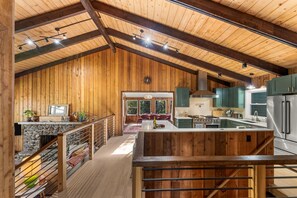 A spacious kitchen with wooden beams, a central island, and a view to a dining area.