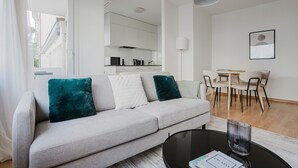A modern living room with a grey sofa, teal cushions, a black coffee table, and a dining area with a white table and chairs.