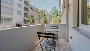 A balcony with a small table and chairs, a view of neighboring buildings, and a clear sky.