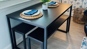 Un coin repas avec une table en bois foncé, des sets de table en fibres tressées et une petite plante en pot.