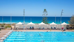 A swimming pool with clear blue water, surrounded by white canopies and lounge chairs, with a view of the ocean and clear sky. - Scarborough Beach Front Resort - Shell Thirteen (Scarborough)