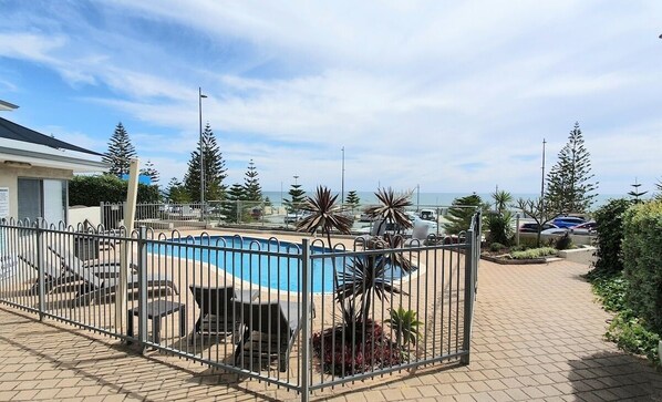Ein Poolbereich im Freien, umzäunt mit Liegestühlen und Blick auf den Ozean.