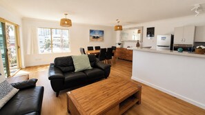 Un salon moderne avec un canapé en cuir noir, une table basse en bois et un coin repas comprenant une table et des chaises en bois.