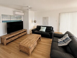 Un salon équipé d’un téléviseur, de meubles en bois, d’un canapé noir et d’un ventilateur de plafond.