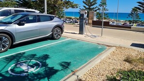 Un espace de stationnement équipé de bornes de recharge pour véhicules électriques, offrant une vue dégagée sur l’océan, et un parking où sont garées des voitures.