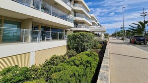 Un immeuble moderne à plusieurs étages, doté de balcons, d’un jardin aménagé et surplombant un ciel dégagé.