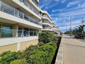 Un edificio moderno de varios pisos con balcones, un jardín ajardinado y un cielo despejado.