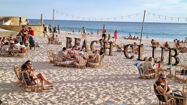 Un club de plage avec des fauteuils et des tables en osier disposés sur le sable, offrant une vue sur la mer.
