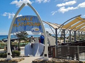 A Whale Playground entrance with a blue and yellow sign, supported by a metal arch structure.