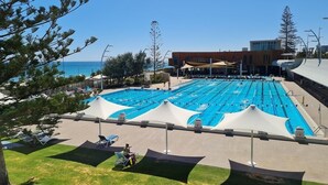 Une piscine dotée de plusieurs couloirs, entourée de chaises longues et de parasols, avec un bâtiment en arrière-plan.