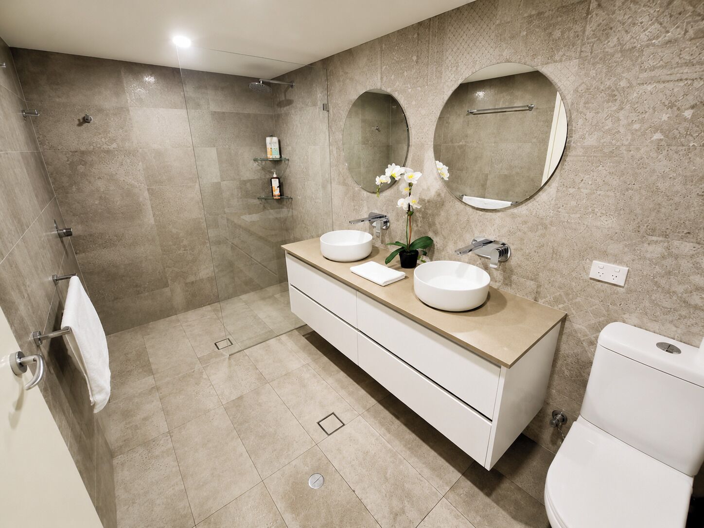 A modern bathroom with two sinks, a toilet, and a shower area.