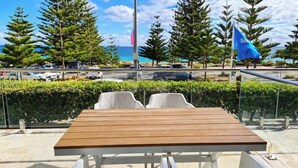A wooden table with two chairs, a glass railing, and a view of the ocean and trees. - Sunset Shores Scarborough (Scarborough)