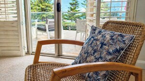 A wicker chair with a leaf-patterned pillow in a room with a glass door leading to an outdoor area. - Sunset Shores Scarborough (Scarborough)