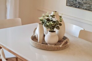 A table with a woven tray holding three white vases and a potted plant. - Beach Break @ iconic Scarborough (Scarborough)