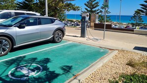 Un espace de stationnement équipé de bornes de recharge pour véhicules électriques, offrant une vue dégagée sur l’océan, et comprenant une place de stationnement réservée aux véhicules électriques.