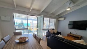 Un salon moderne avec une table à manger en bois, un canapé noir et un téléviseur fixé au mur.