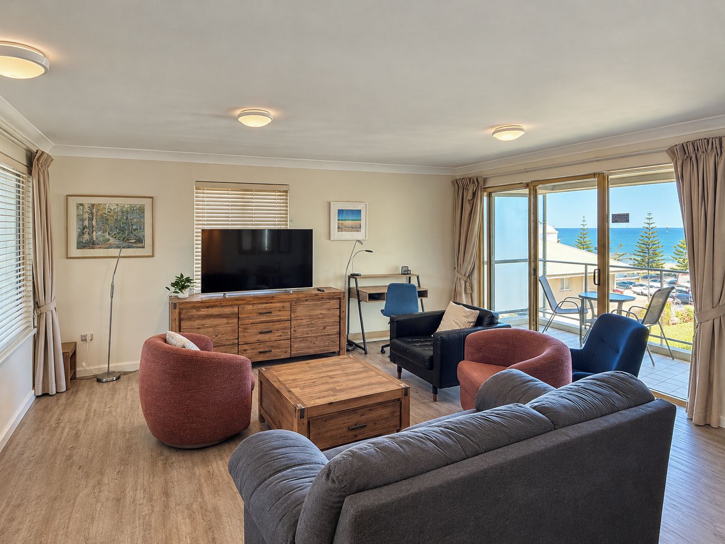 Una sala de estar moderna con un televisor de pantalla plana, muebles de madera y vista al mar.