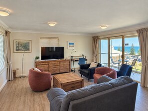 A modern living room with a flat-screen TV, wooden furniture, and a view of the sea. - Sandcastles at the Beach – Outstanding Location! (Scarborough)