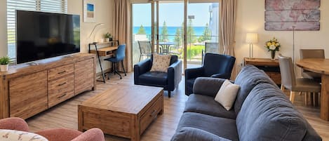 A modern living room with a flat-screen TV, a sofa, a coffee table, and a dining area with a table and chairs.