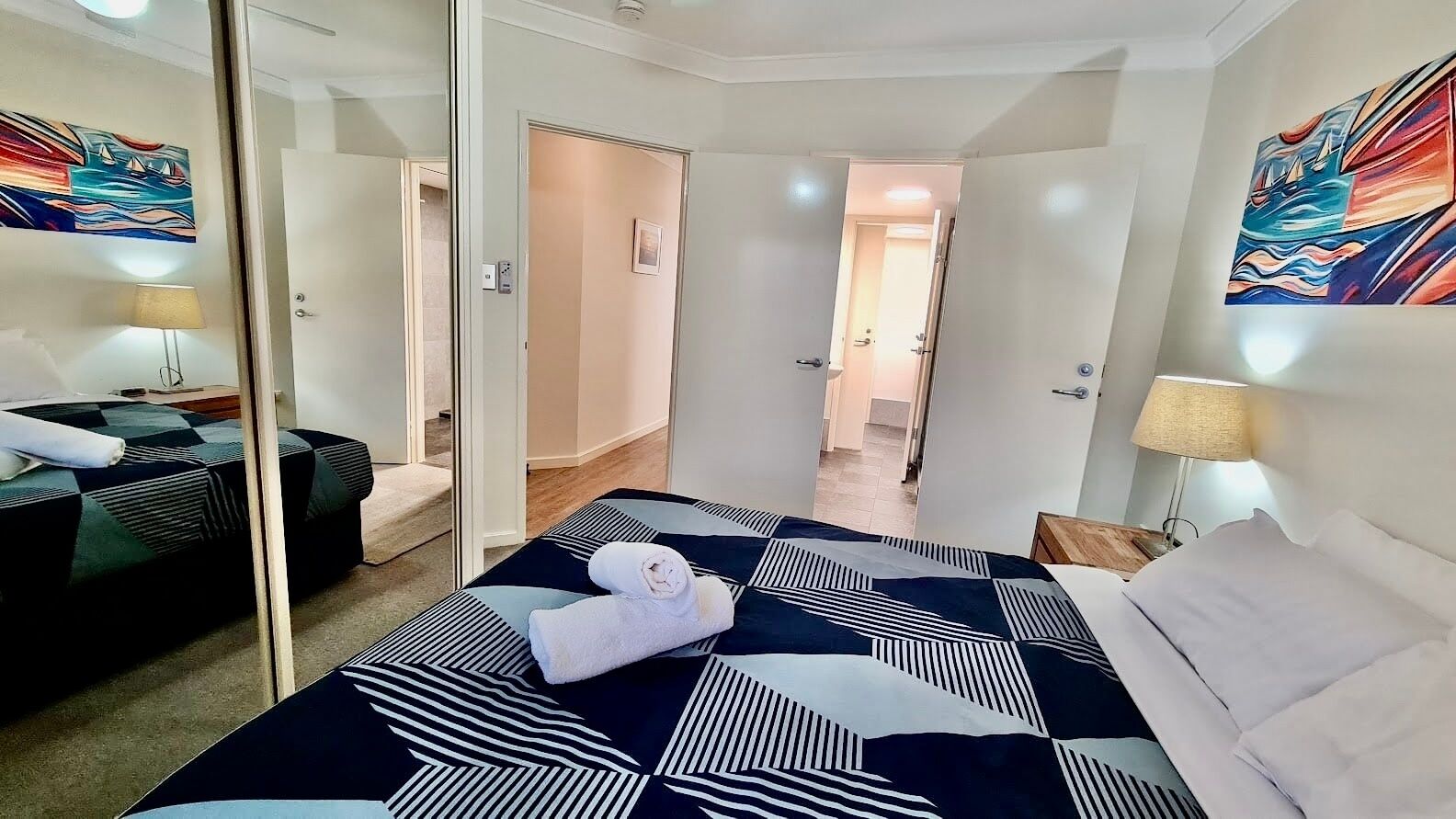 Ein Hotelzimmer mit einem großen Bett, einem Nachttisch, einem Spiegel und einem Bild an der Wand.