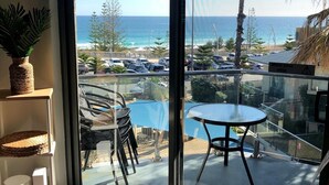 A balcony with a glass door, a small table, and chairs. There is a view of the ocean and a parking lot with cars. - Scarborough Sunset on Esplanade (Scarborough)
