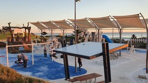 A playground with slides and climbing structures, surrounded by shaded areas and benches. - Scarborough Sunset on Esplanade (Scarborough)