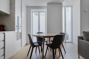 Enjoy meals in this dining area with a wooden table and four chairs, surrounded by large windows and a comfortable sofa.