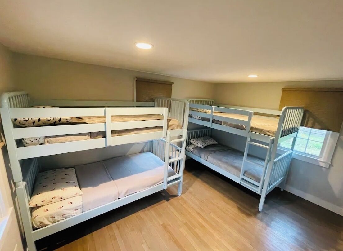 A room with three bunk beds, wooden flooring, and a window with blinds.