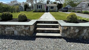 Un camino de entrada residencial que lleva a una casa con muro de piedra y escalones.