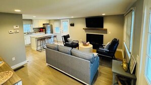 Una sala de estar moderna con un sofá gris, una chimenea y una cocina al fondo.