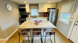 Una cocina moderna con una isla de mármol, cuatro taburetes de bar, un refrigerador de acero inoxidable y un reloj en la pared.