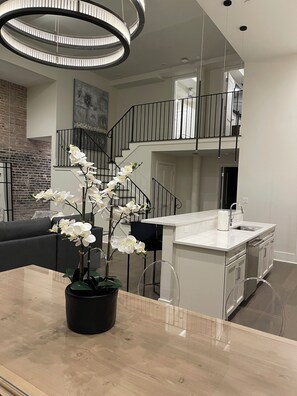 Una cocina moderna con una isla central, un comedor con un sofá negro y una escalera que sube a un nivel superior.