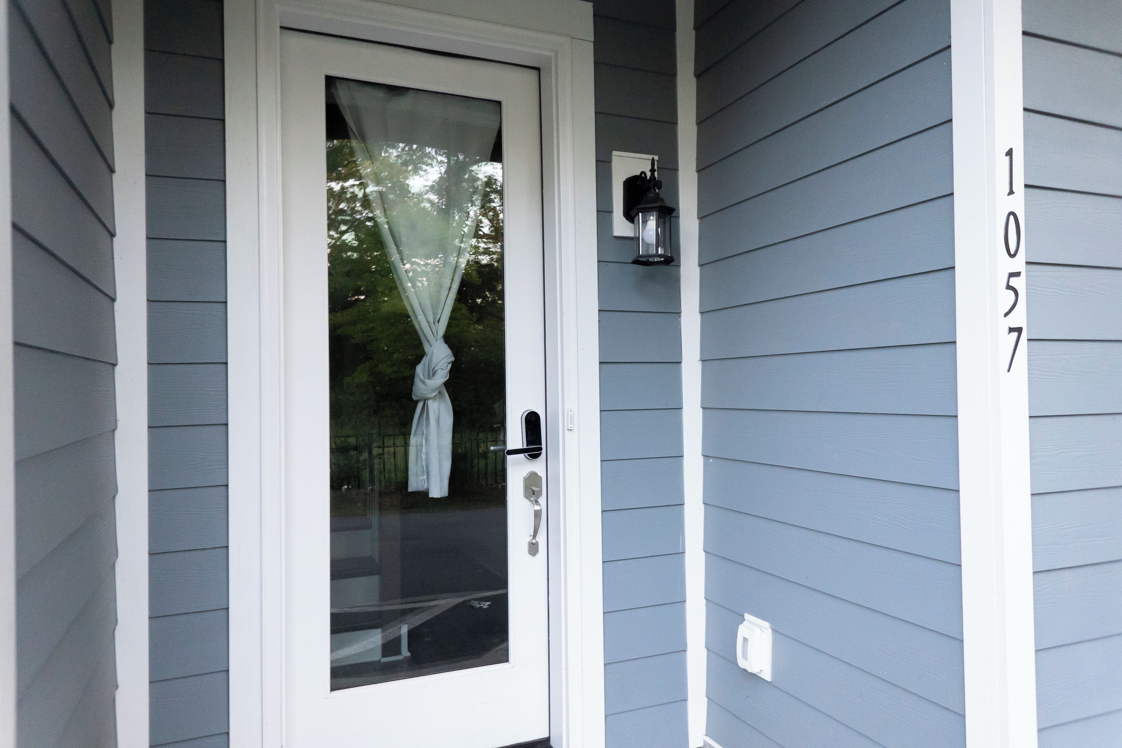 A front door with a glass panel, a number '1057' on the wall, and a wall-mounted light fixture.