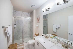 Ein Badezimmer mit Duschkabine, Toilette, Waschbecken mit Spiegel und Handtuchhalter.