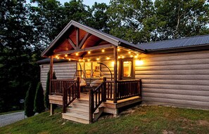Une cabane en rondins dotée d’une véranda, d’une balustrade en bois et de guirlandes lumineuses.