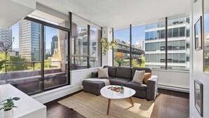 Una sala de estar moderna con un sofá gris, una mesita de centro blanca y un ventanal con vistas a la ciudad.