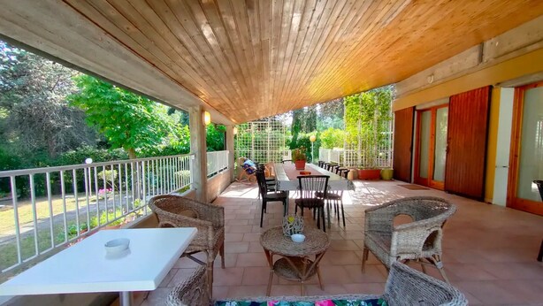 Un patio al aire libre con mobiliario de mimbre, una mesa blanca y vistas a la vegetación.