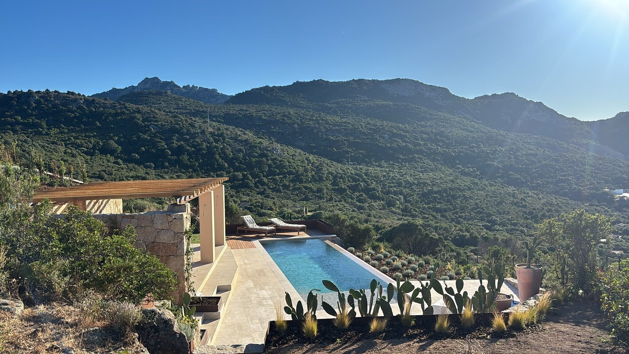 A pool with a wooden pergola, cacti, and a mountainous backdrop.