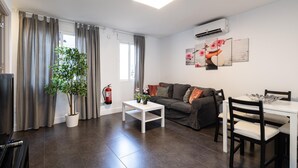 A modern living room with a sofa, coffee table, and dining area. There is a potted plant, a fire extinguisher, and artwork on the wall. - Holidays2Malaga Los Negros RoofTop for common use (Málaga)