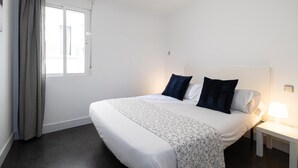 A bedroom with a bed, a ceiling fan, a nightstand with a lamp, and a window with curtains. - Holidays2Malaga Los Negros RoofTop for common use (Málaga)