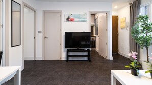 A modern living room with a flat-screen TV on a black stand, a dining table, and a potted plant. - Holidays2Malaga Los Negros RoofTop for common use (Málaga)