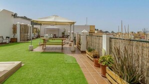 A patio area with a table and chairs under a canopy, surrounded by a wooden fence and potted plants. - Holidays2Malaga Los Negros RoofTop for common use (Málaga)