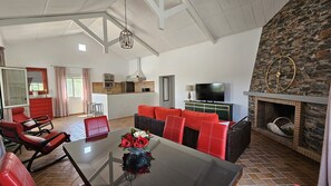Ett rymligt vardagsrum med en öppen spis i sten, ett matbord med röda stolar, ett kök med modern design och en stor TV.