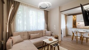 A modern living room with a sofa, a small table with a cake, and a dining area with chairs and a table. - Second home Next to Sea Garden (Varna)