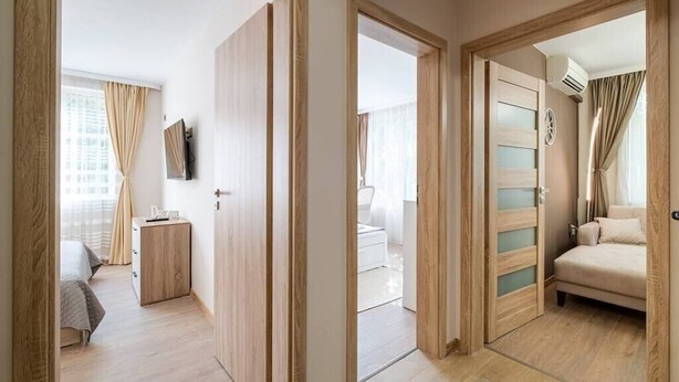 A modern hotel room with a wooden floor, a bed, a desk, and a TV. - Second home Next to Sea Garden (Varna)