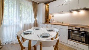A modern kitchen with white cabinets, a built-in oven, and a dining area with a round table and chairs. - Second home Next to Sea Garden (Varna)