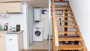 Une cuisine compacte équipée d’un lave-linge, d’un petit réfrigérateur et d’une échelle en bois menant à une mezzanine.